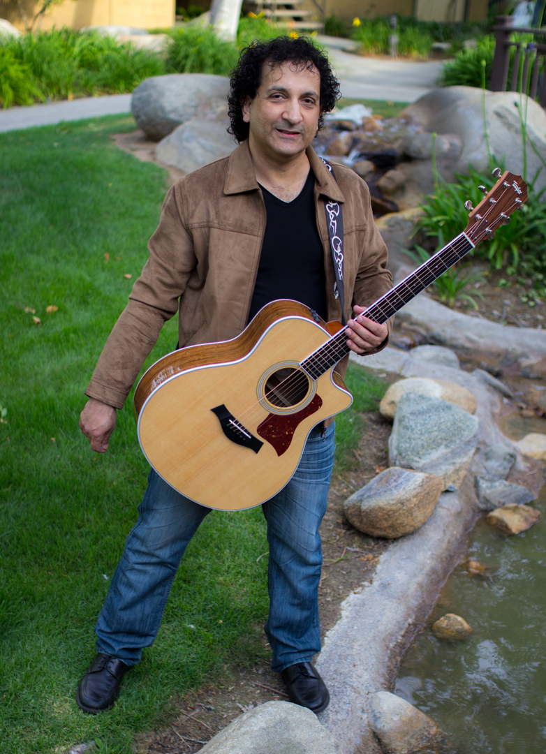a man standing on grass with his guitar near a small water fall