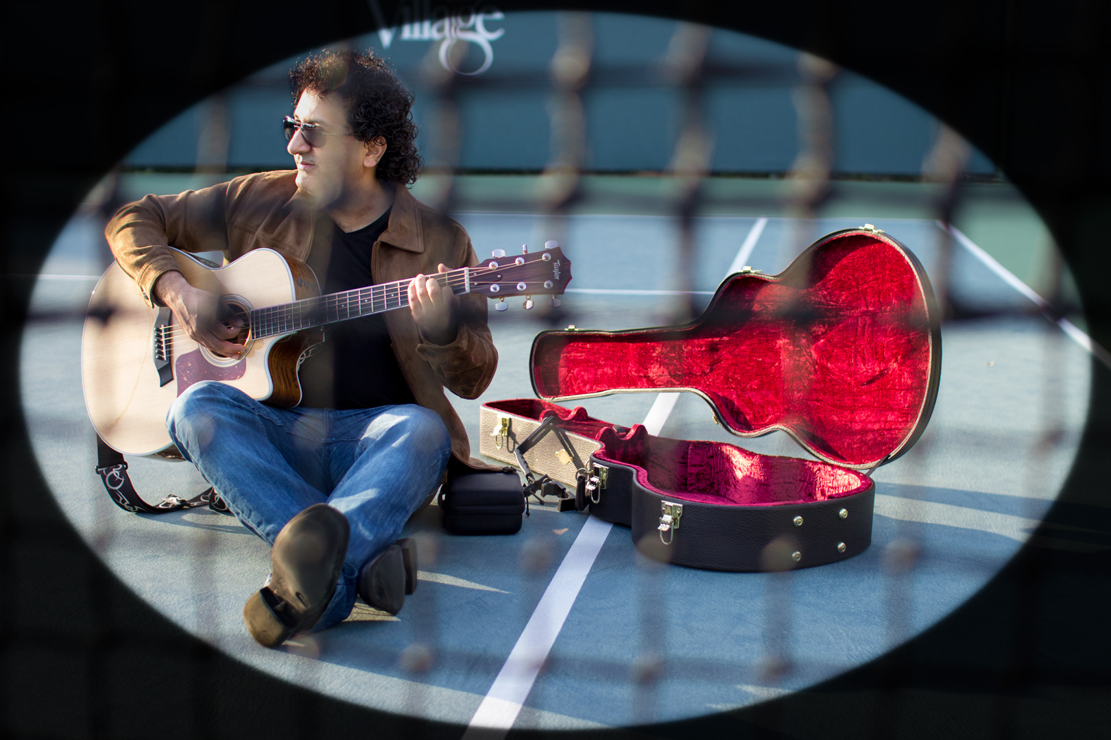 a man sitting on a tennis court playing guitar alongside is a guitar case