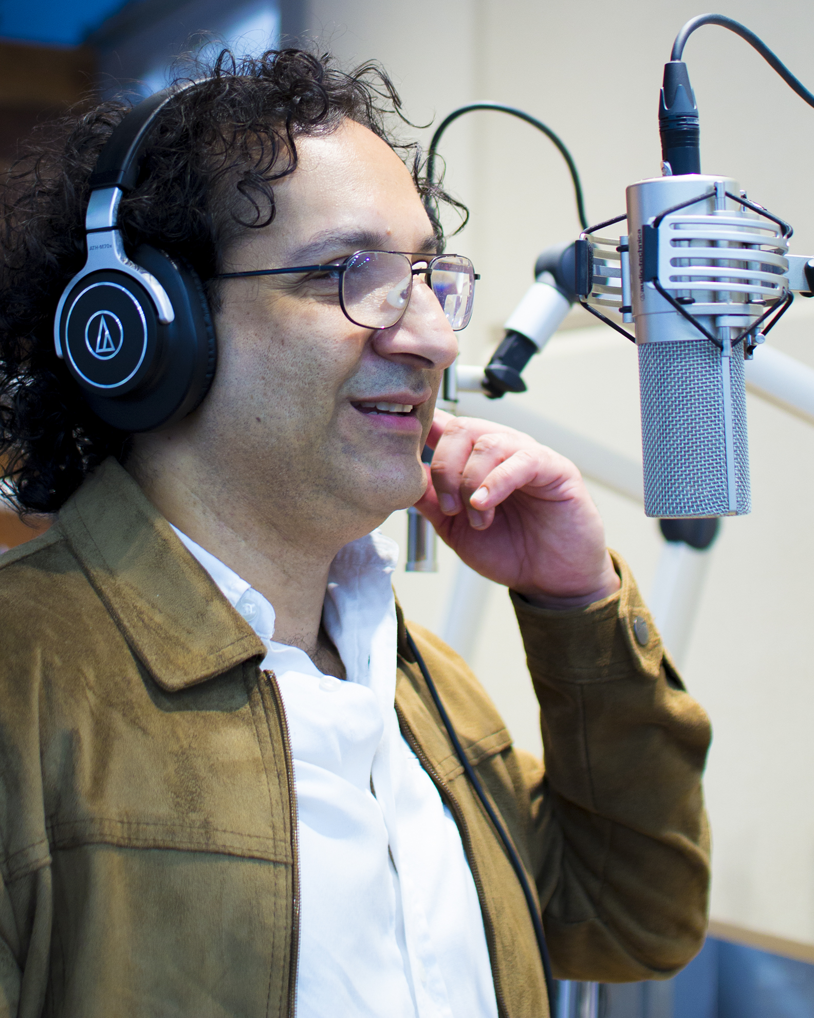 man with headphones on singing in front of a condenser microphone in a recording studio